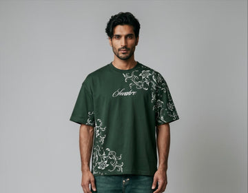 Man wearing a green t-shirt with white floral patterns and text on a gray background
